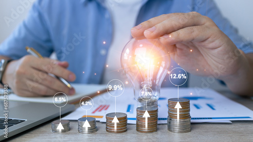 Interest rate and dividend concept.Businessman touch light bulb to idea stacking coins and calculating with percentage for interest rating. investment, fund and stock market.