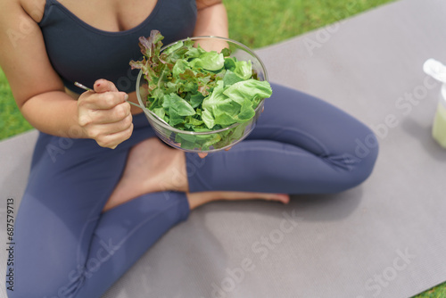 Beautiful confident Fitness asian woman eating healthy salad after workout. training yoga in green park