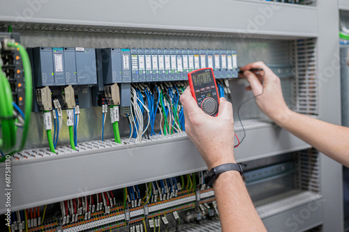 Electrician checks voltage in PLC card with meassuring instrument in electrical cabinet photo