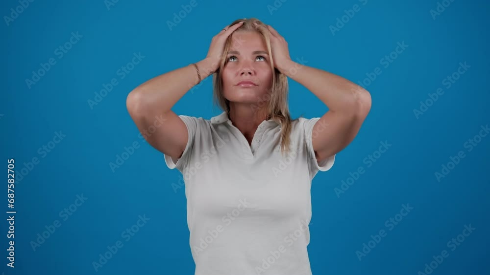 Shocked young woman is grabbing her head looking mad and upset standing isolated over a blue background in the studio Shocked young woman is grabbing her head looking mad and upset standing isolated over a blue background in the studio