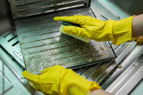 Housekeeping put stained filters of cooker hood in sink before cleaning it by sponge. photo