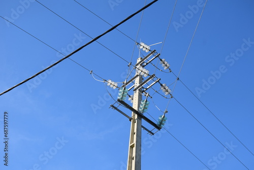 Utility pole with electricity cables seen from the ground, clear sky above