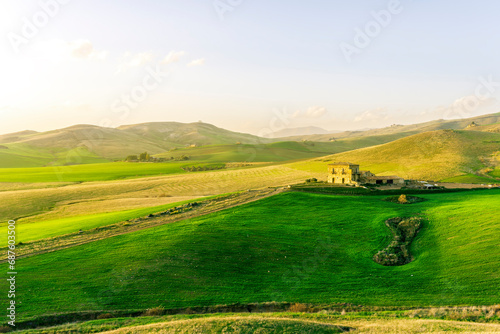 countryside sunset in green hills of spring fields with old castle farm and mountains on background of evening landscape