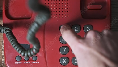 Calling 911. Top view on an old vintage red telephone, man hand presses the dial buttons. Dialing emergency number on a retro home landline telephone. Number buttons on retro push dial phone. Close-up photo