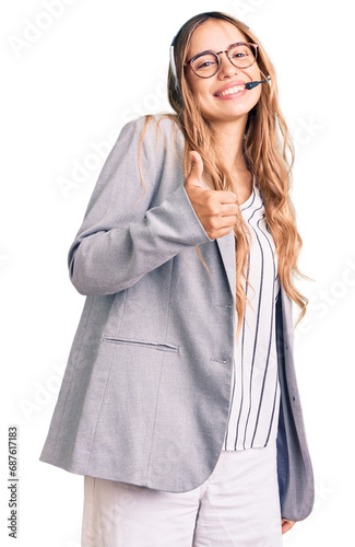 Young beautiful blonde woman wearing call center agent headset doing happy thumbs up gesture with hand. approving expression looking at the camera showing success. photo