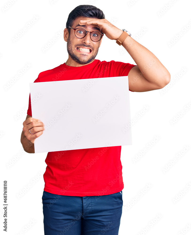 Young hispanic man holding blank empty banner stressed and frustrated with hand on head, surprised and angry face Young hispanic man holding blank empty banner stressed and frustrated with hand on head, surprised and angry face