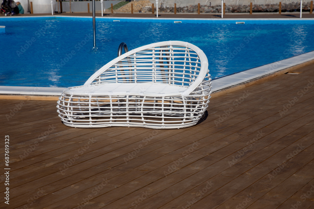 Modern white rattan furniture to create an outdoor pool in living room by sea. Luxurious swimming pool with white fashionable sun loungers on the beach. Landscape, interior for luxury holidays Modern white rattan furniture to create an outdoor pool in living room by sea. Luxurious swimming pool with white fashionable sun loungers on the beach. Landscape, interior for luxury holidays