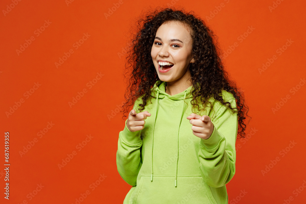 Young leader woman of African American ethnicity she wear green hoody casual clothes point index finger camera on you motivating encourage isolated on plain red orange background. Lifestyle concept. Young leader woman of African American ethnicity she wear green hoody casual clothes point index finger camera on you motivating encourage isolated on plain red orange background. Lifestyle concept.