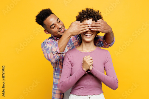 Young couple two friend family man woman of African American ethnicity wear purple casual clothes together close eyes with hands play guess who or hide and seek isolated on plain yellow background.