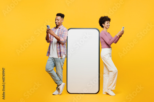 Full body side view young couple two friend family man woman wear purple casual clothes together big huge blank screen mobile cell phone with area using smartphone isolated on plain yellow background