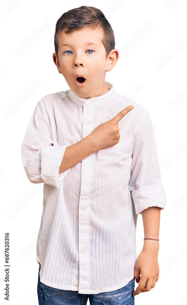 Cute blond kid wearing elegant shirt surprised pointing with finger to the side, open mouth amazed expression. Cute blond kid wearing elegant shirt surprised pointing with finger to the side, open mouth amazed expression.