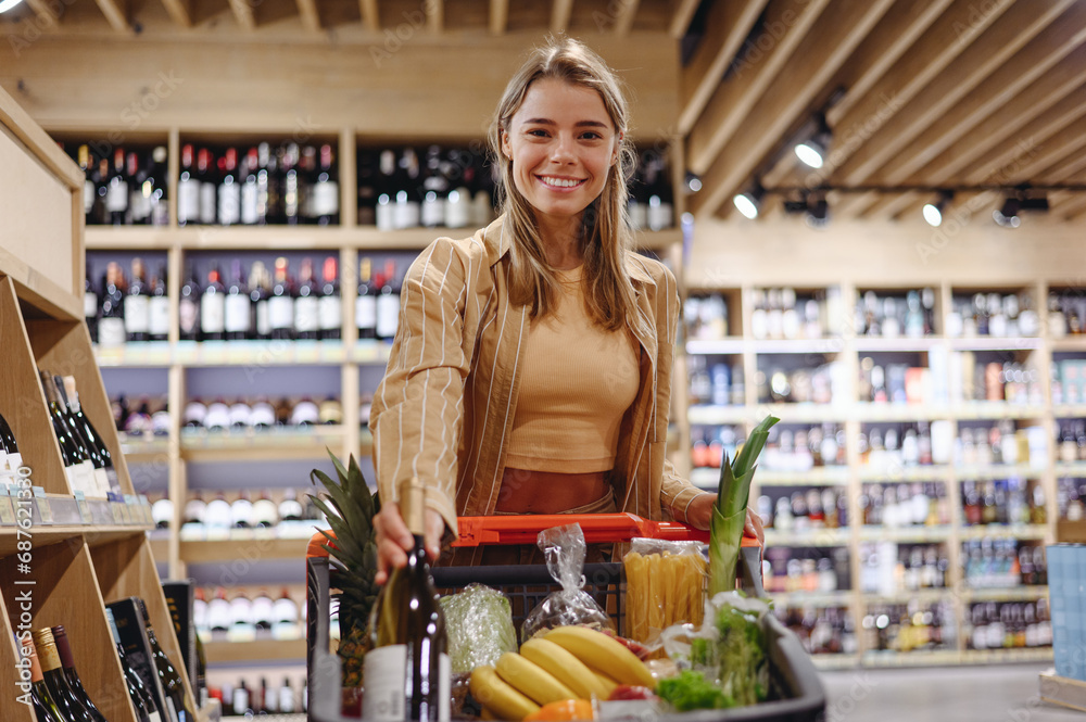 Young customer woman wears casual clothes put bottle of wine shopping at supermaket store grocery shop buying with trolley cart choose products inside hypermarket. Purchasing food gastronomy concept.