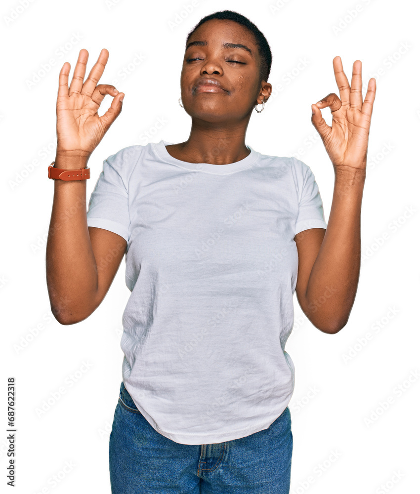Young african american woman wearing casual white t shirt relaxed and smiling with eyes closed doing meditation gesture with fingers. yoga concept. Young african american woman wearing casual white t shirt relaxed and smiling with eyes closed doing meditation gesture with fingers. yoga concept.