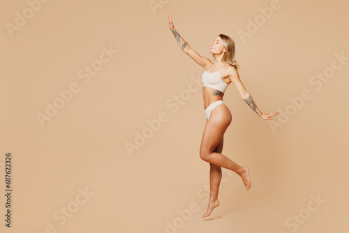 Full body side view young nice lady woman with slim body perfect skin wearing nude top bra lingerie stand raise up hands pov fly isolated on plain pastel beige background. Lifestyle diet fit concept.