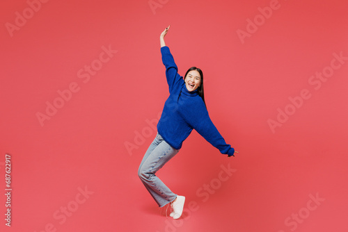 Full body side view fun young woman of Asian ethnicity she wearing blue sweater casual clothes stand on toes with outstretched hands leaning back dance isolated on plain pastel pink background studio. photo
