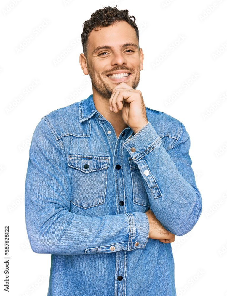 Young hispanic man wearing casual denim jacket looking confident at the camera with smile with crossed arms and hand raised on chin. thinking positive. Young hispanic man wearing casual denim jacket looking confident at the camera with smile with crossed arms and hand raised on chin. thinking positive.