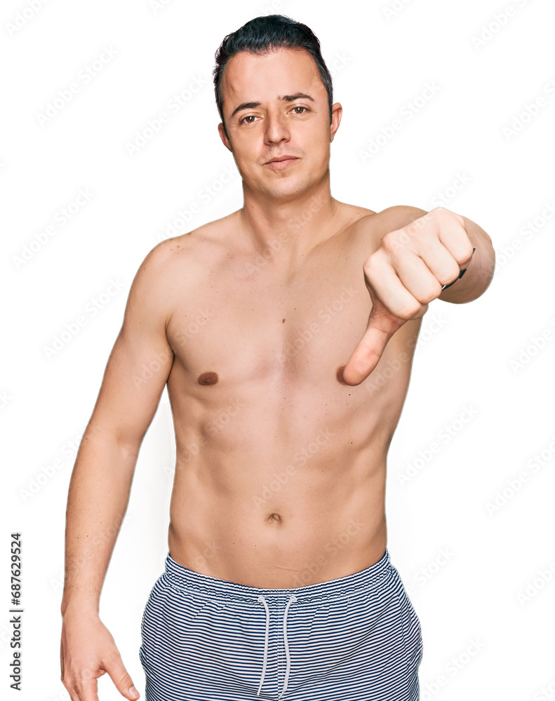 Handsome young man wearing swimwear shirtless looking unhappy and angry showing rejection and negative with thumbs down gesture. bad expression.