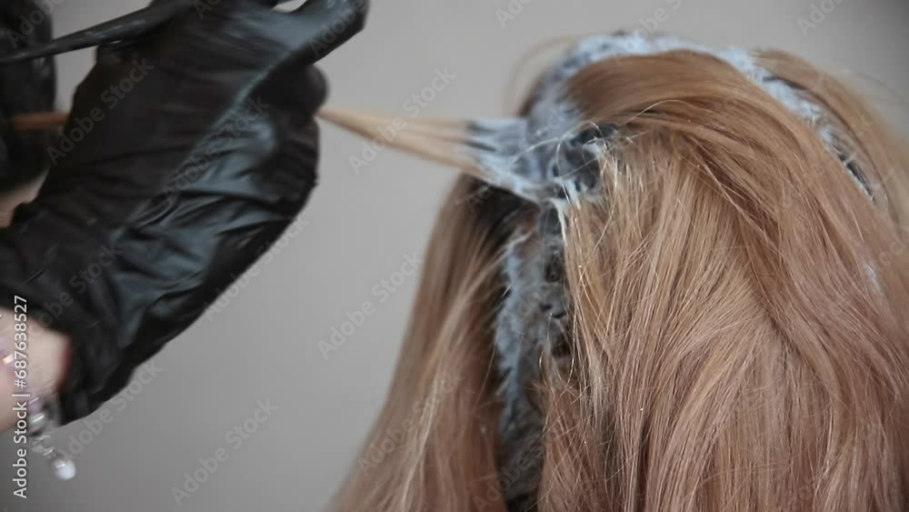 the master of hair coloring applies paint with brush to the head of red-haired woman, close-up