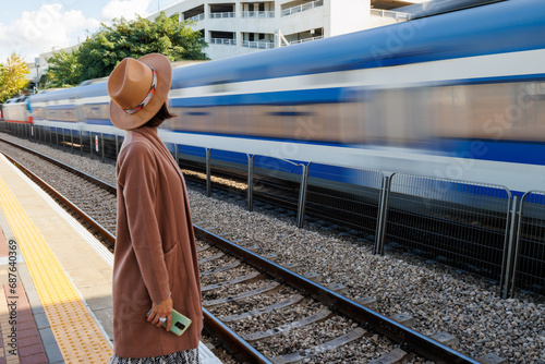 Girl at the railway station. A young woman in a coat and hat stands on the station platform and looks at the train.