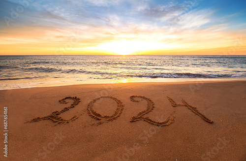 Happy New Year 2024 ocean sunrise on the beach. Written text on the sea beach at sunrise.