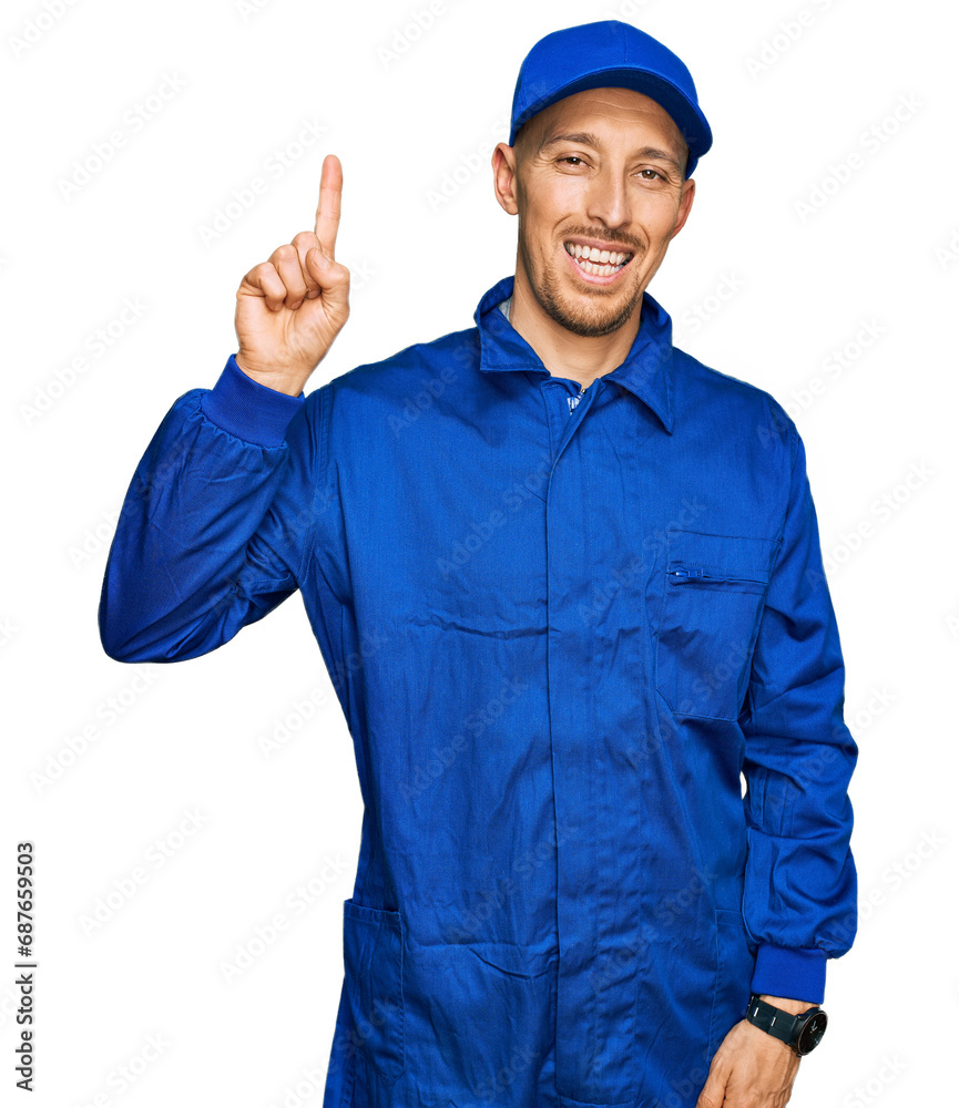 Bald man with beard wearing builder jumpsuit uniform pointing finger up with successful idea. exited and happy. number one.