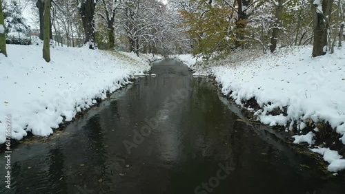 Fly over winter city stream calm river covered in snow, drone