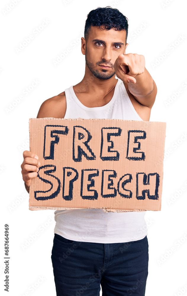 Young hispanic man holding free speech banner pointing with finger to the camera and to you, confident gesture looking serious Young hispanic man holding free speech banner pointing with finger to the camera and to you, confident gesture looking serious