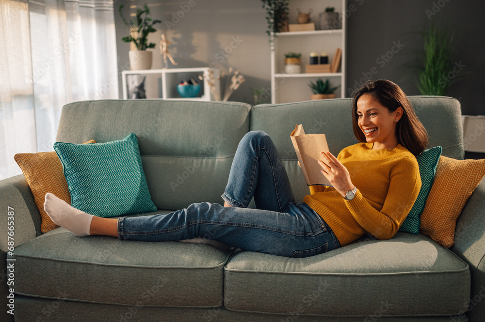 Obraz premium A cheerful woman is relaxing at home and reading a book.