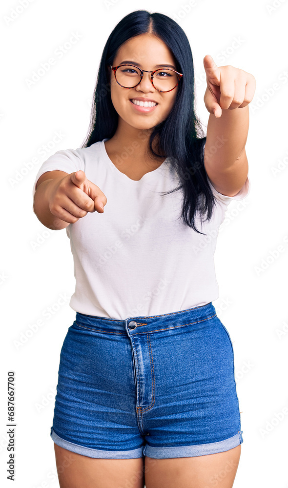 Young beautiful asian girl wearing casual clothes and glasses pointing to you and the camera with fingers, smiling positive and cheerful Young beautiful asian girl wearing casual clothes and glasses pointing to you and the camera with fingers, smiling positive and cheerful