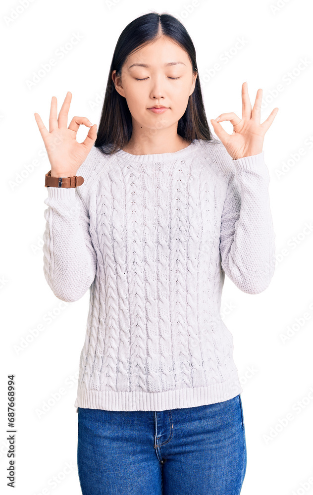Young beautiful chinese woman wearing casual sweater relaxed and smiling with eyes closed doing meditation gesture with fingers. yoga concept. Young beautiful chinese woman wearing casual sweater relaxed and smiling with eyes closed doing meditation gesture with fingers. yoga concept.