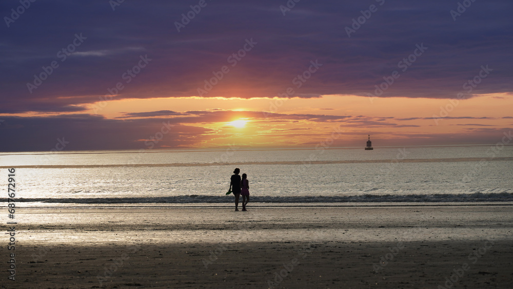 Two people walk on the beach at a spectacular sunset