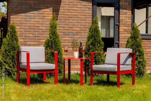 two red armchairs with gray pillows on green grass against the background of a brick wall