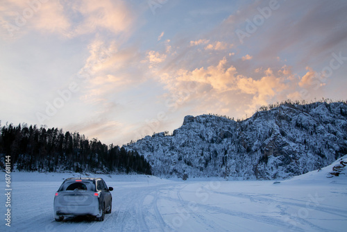 Winter travel. The car against the backdrop of a winter landscape, white snow, sunset sky, mountains in the background.