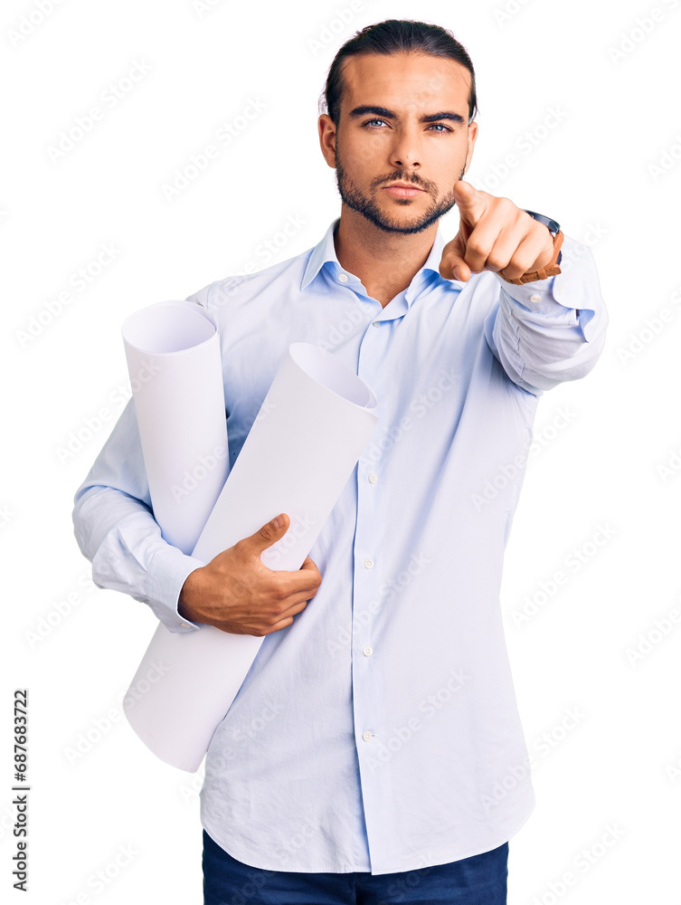 Young handsome man holding paper blueprints pointing with finger to the camera and to you, confident gesture looking serious Young handsome man holding paper blueprints pointing with finger to the camera and to you, confident gesture looking serious