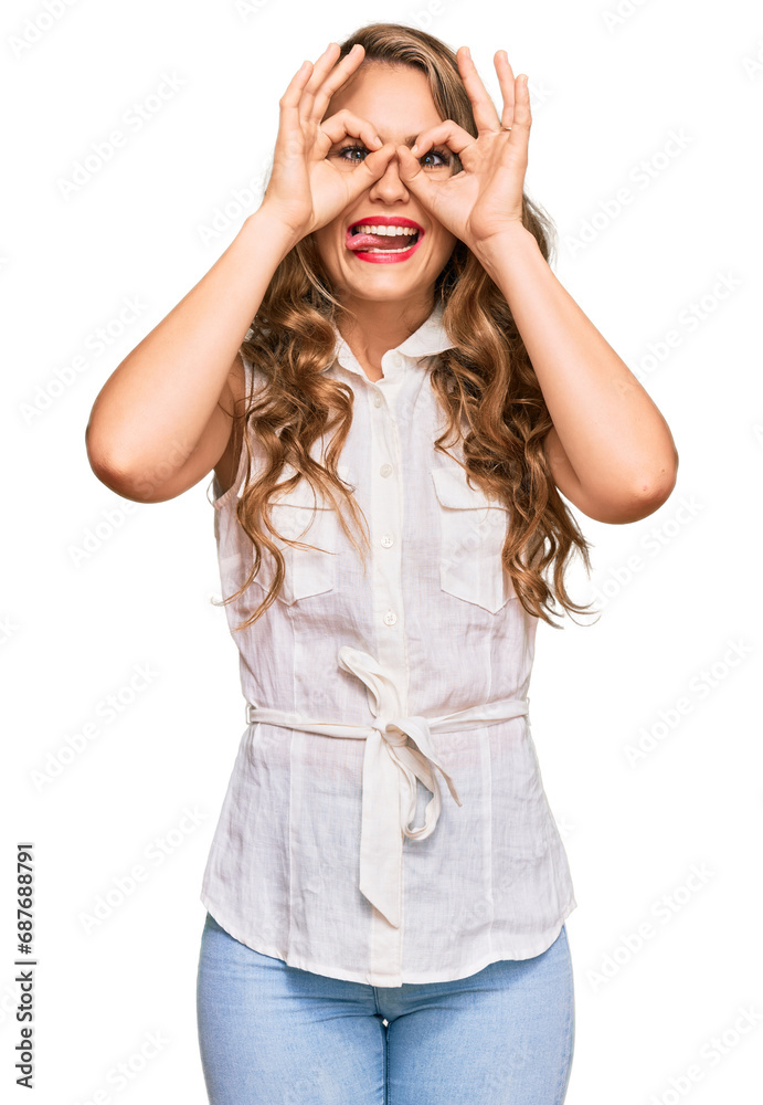Young blonde girl wearing casual clothes doing ok gesture like binoculars sticking tongue out, eyes looking through fingers. crazy expression. Young blonde girl wearing casual clothes doing ok gesture like binoculars sticking tongue out, eyes looking through fingers. crazy expression.