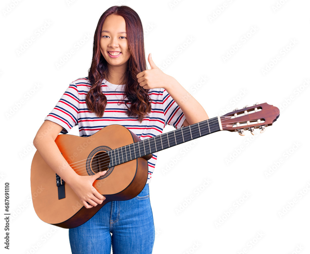 Young beautiful chinese girl playing classical guitar smiling happy and positive, thumb up doing excellent and approval sign Young beautiful chinese girl playing classical guitar smiling happy and positive, thumb up doing excellent and approval sign