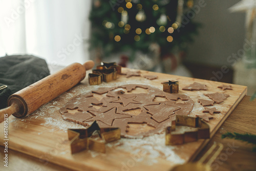 Gingerbread dough with golden cutters, rolling pin, cooking spices and festive decorations on wooden table against stylish christmas tree. Making christmas gingerbread cookies, holiday time