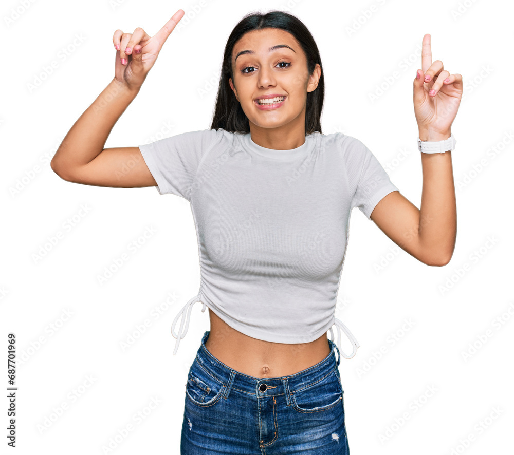 Young hispanic girl wearing casual white t shirt smiling amazed and surprised and pointing up with fingers and raised arms. Young hispanic girl wearing casual white t shirt smiling amazed and surprised and pointing up with fingers and raised arms.