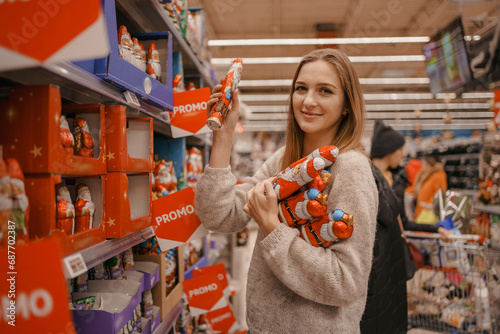 Stack of Chocolate Santa Clauses. Christmas time. A young woman chooses a gift set for Christmas to a child on a supermarket shelf.