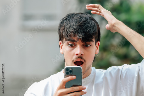 Photos portrait of young man looking at mobile phone surprised