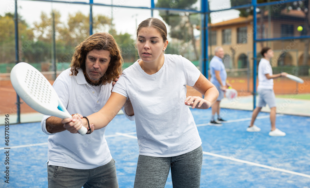 Portrait of concentrated male trainer teaching young woman playing padel outdoor