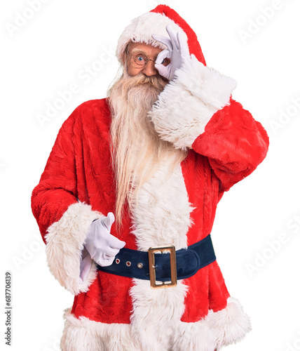 Old senior man with grey hair and long beard wearing traditional santa claus costume doing ok gesture with hand smiling, eye looking through fingers with happy face.
