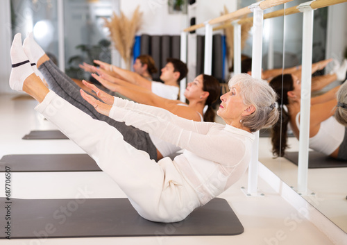 Elderly athletic woman performs pilates exercises in gym