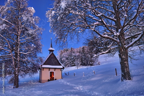 Kapelle im Winter bei Abenddämmerung und Neuschnee in romantischer Stimmung mit Kerzenlicht