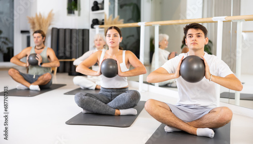 Group of cheerful sports people of different ages practicing pilates with a ball in the gym of a modern fitness studio.