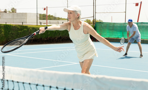 Elderly active woman bouncing ball in tennis game on court with racket © JackF