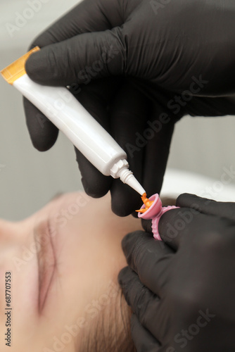 Microblading artist  in a black gloves mixing pigment in ink ring cup. Close-up of pigment ring container and ink for eyebrow tattoo. Beauty procedure preparation.