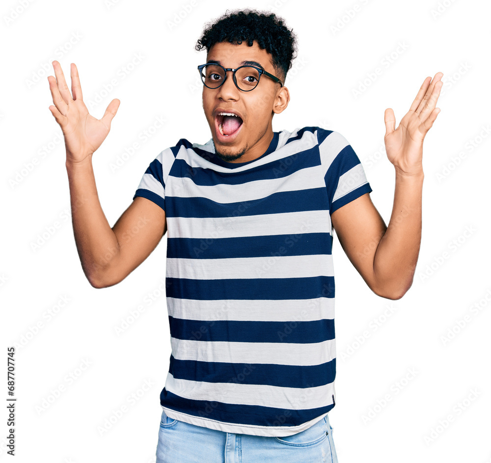 Young african american man wearing casual clothes and glasses celebrating crazy and amazed for success with arms raised and open eyes screaming excited. winner concept Young african american man wearing casual clothes and glasses celebrating crazy and amazed for success with arms raised and open eyes screaming excited. winner concept