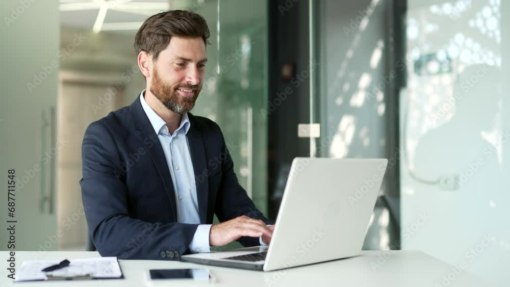 Smiling businessman in a formal suit typing on a laptop while sitting at a workplace in business office. Handsome entrepreneur working on a project on the computer, texting a client or chatting online Smiling businessman in a formal suit typing on a laptop while sitting at a workplace in business office. Handsome entrepreneur working on a project on the computer, texting a client or chatting online
