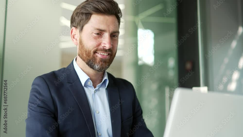Smiling businessman in a formal suit typing on a laptop sitting at a workplace in business office. Handsome entrepreneur working on a project on computer, texting a client or chatting online. Close up Smiling businessman in a formal suit typing on a laptop sitting at a workplace in business office. Handsome entrepreneur working on a project on computer, texting a client or chatting online. Close up